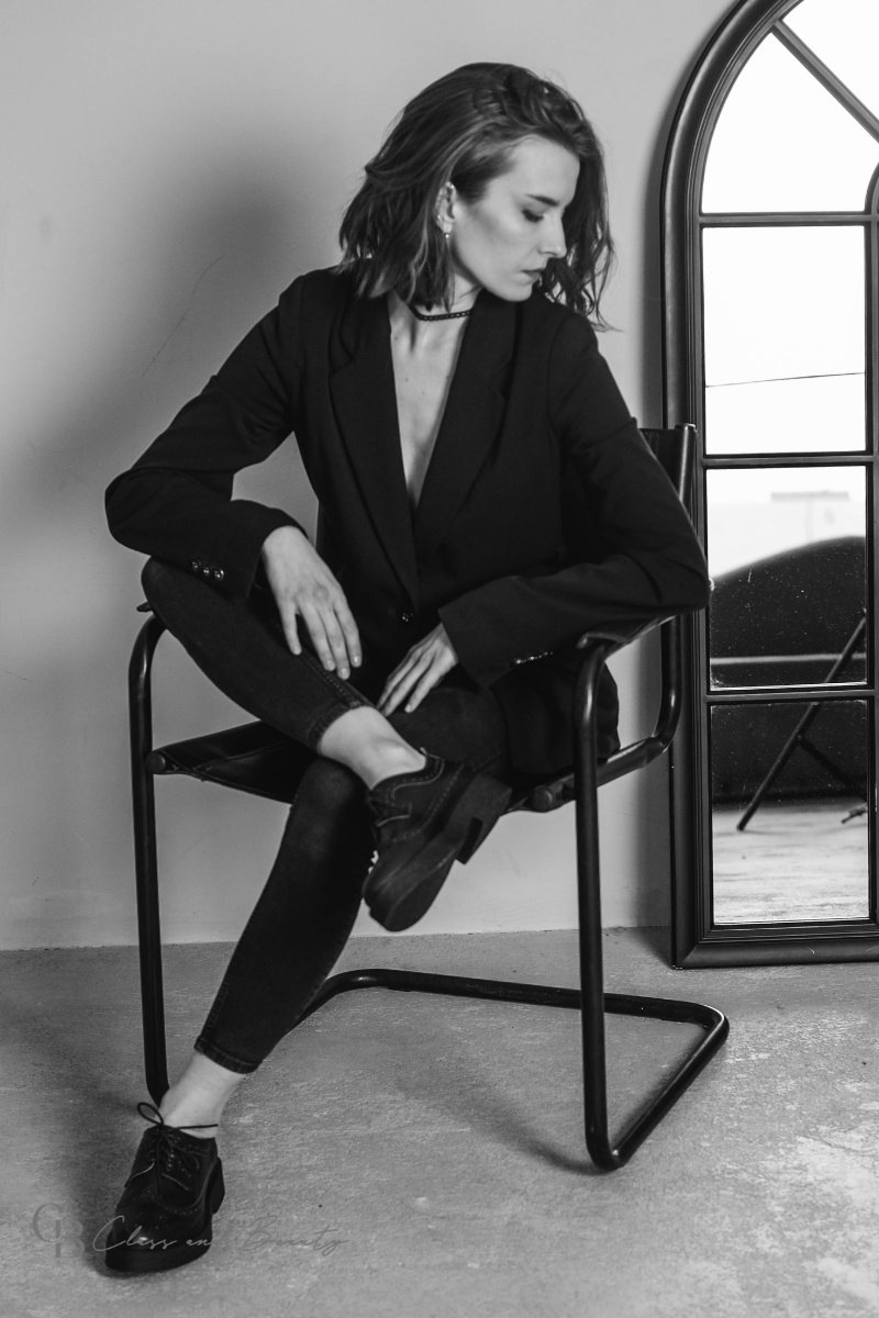 A woman gracefully standing in a white lace camisole and blazer, showcasing her refined classic style