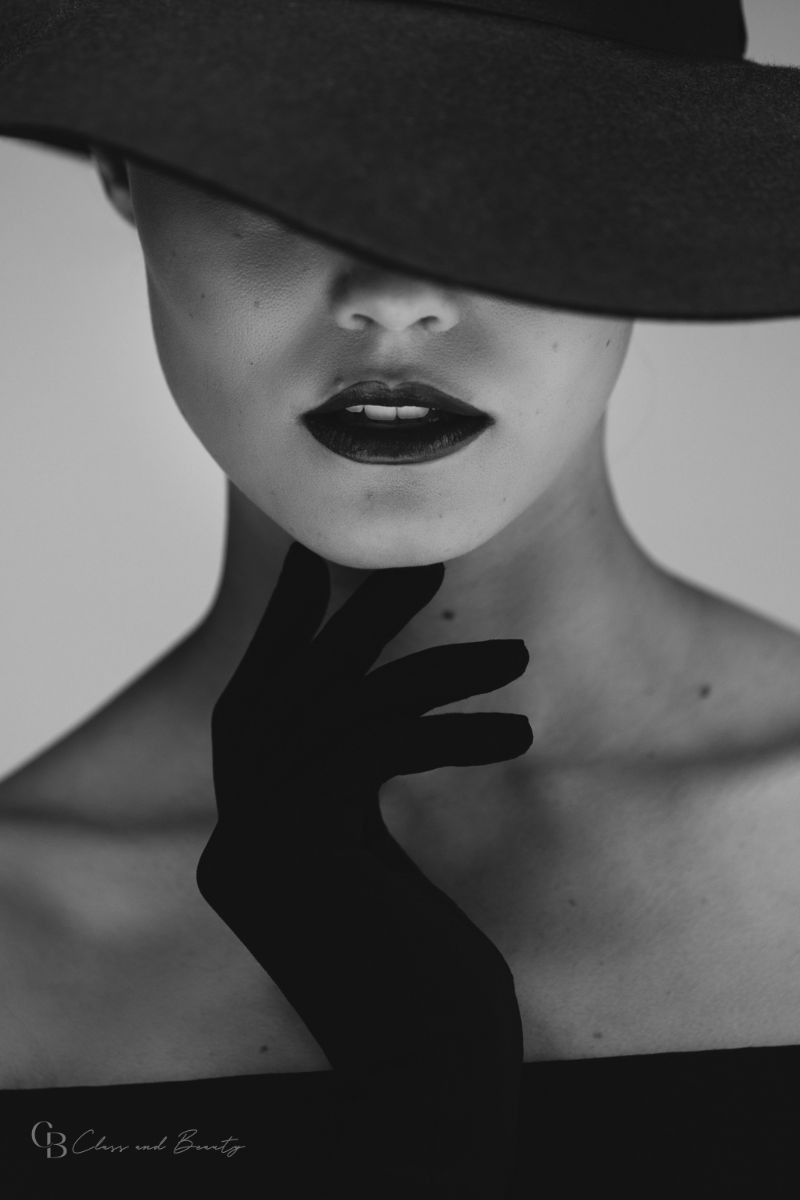 Close-up of a woman wearing black lipstick, gloves, and a large black hat, representing the timeless allure of classic style